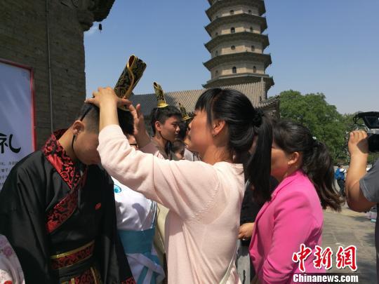 18日,山西省太原市永祚寺,明代文峰塔下,太原市综合高中150名高三生举办成人礼,18名学生代表加冠加笄,祈祷金榜题名。图为父母为子女们加冠、加笄。 李娜 摄