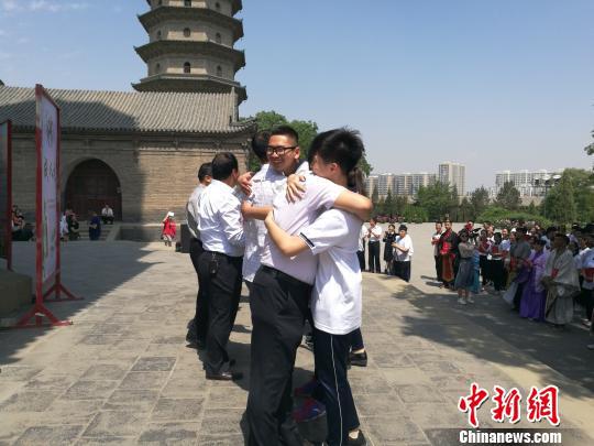 18日,山西省太原市永祚寺,明代文峰塔下,太原市综合高中150名高三生举办成人礼,18名学生代表加冠加笄,祈祷金榜题名。图为学生们和班主任拥抱在一起。 李娜 摄